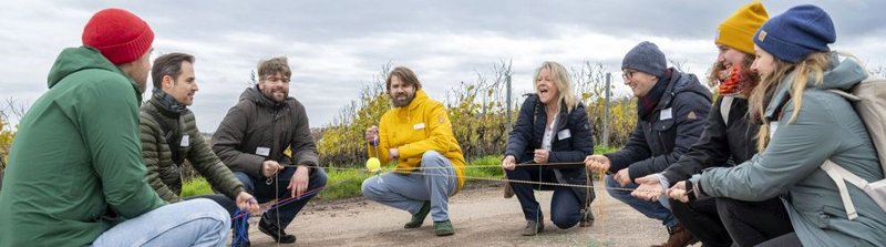 Gruppe Menschen hält Schnüre, die in der Mitte zusammengehen, wie ein Netz und balanciert damit einen Ball